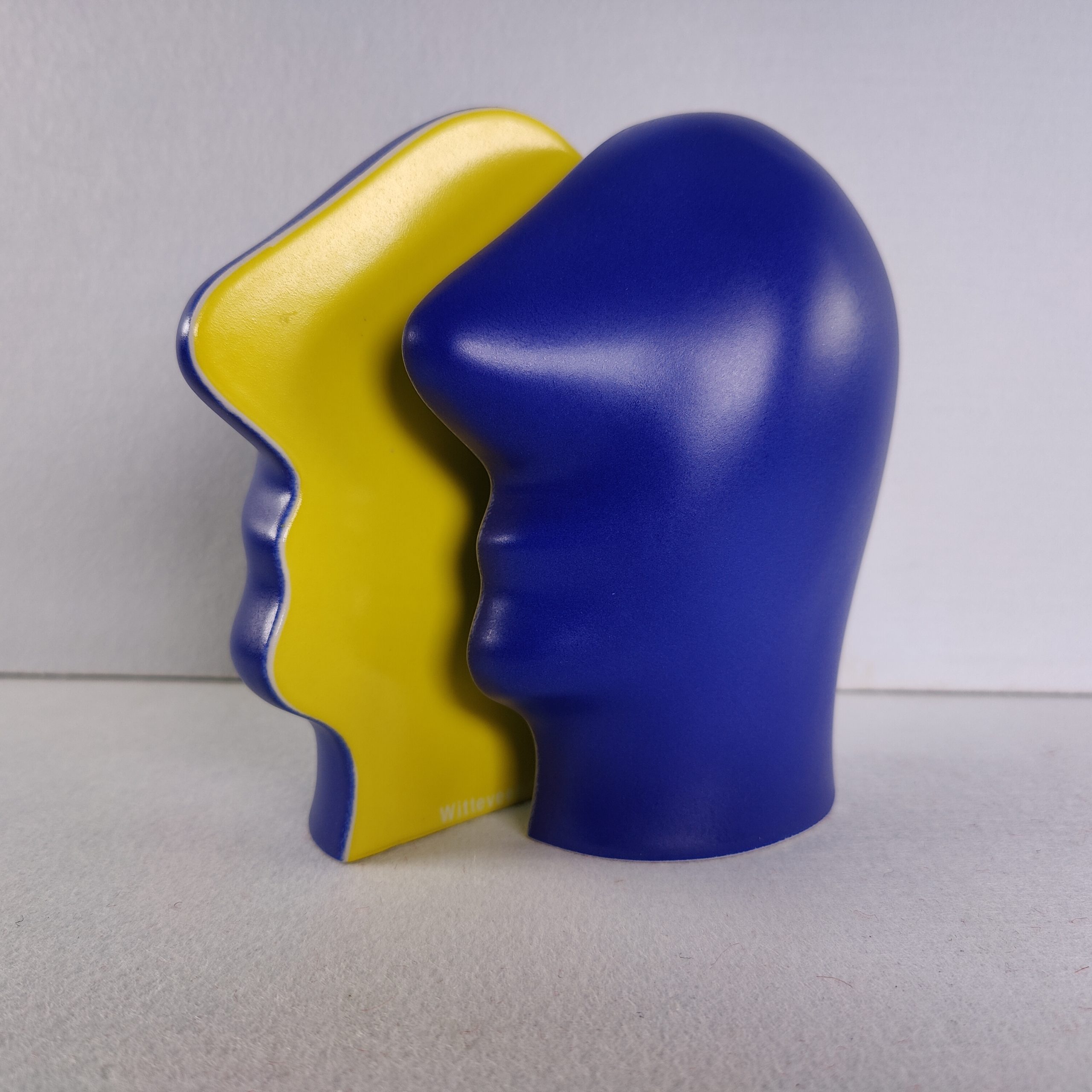 Keramieken beeldje "Split Personality" van Jan Snoeck, vooraanzicht met een blauw hoofd in profiel en daarachter de gele binnenzijde van het tweede deel.