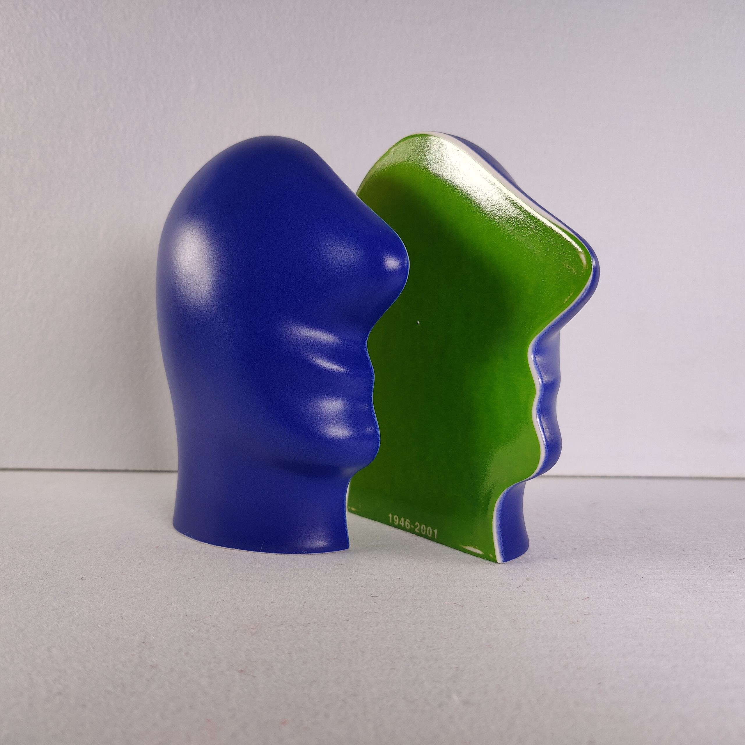 Keramiek beeldje "Split Personality" van Jan Snoeck met een blauw hoofd en een groen tegenstuk, voorzien van de jaartallen 1946-2001