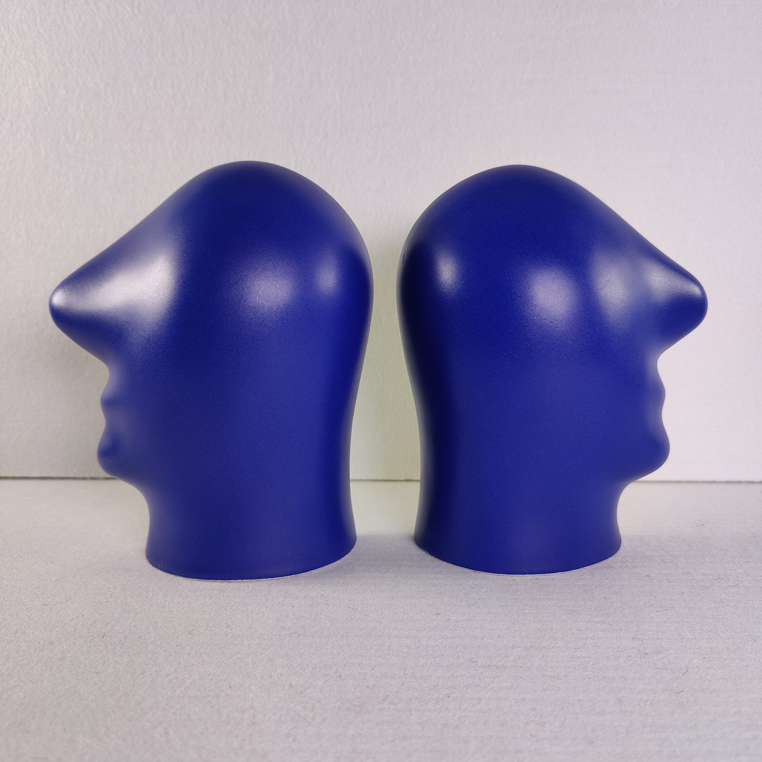 Twee blauwe keramische hoofden van Jan Snoeck naast elkaar als spiegelbeeld, met de ronde zijde naar voren.